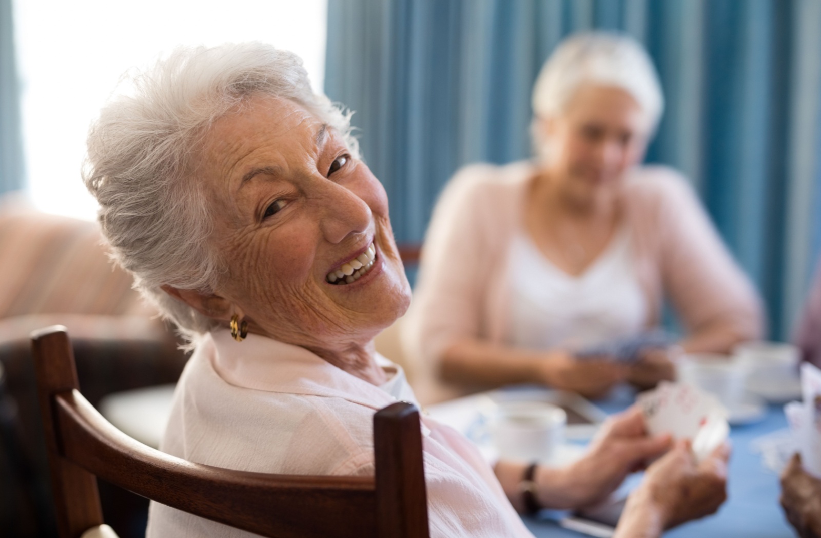 An older adult turning around to smile at the camera during a game of cards in senior living.