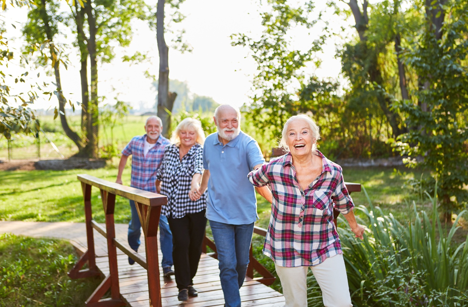 A group of senior laughing and holding hands as they enjoy a walk on a beautiful summer day.