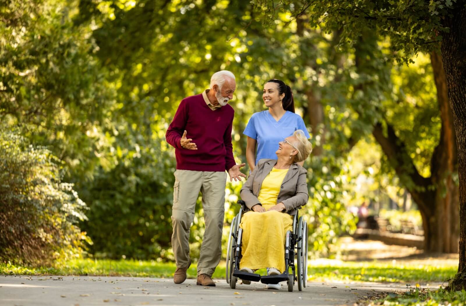 A caregiver assists two people who live in an assisted living community on their walk.
