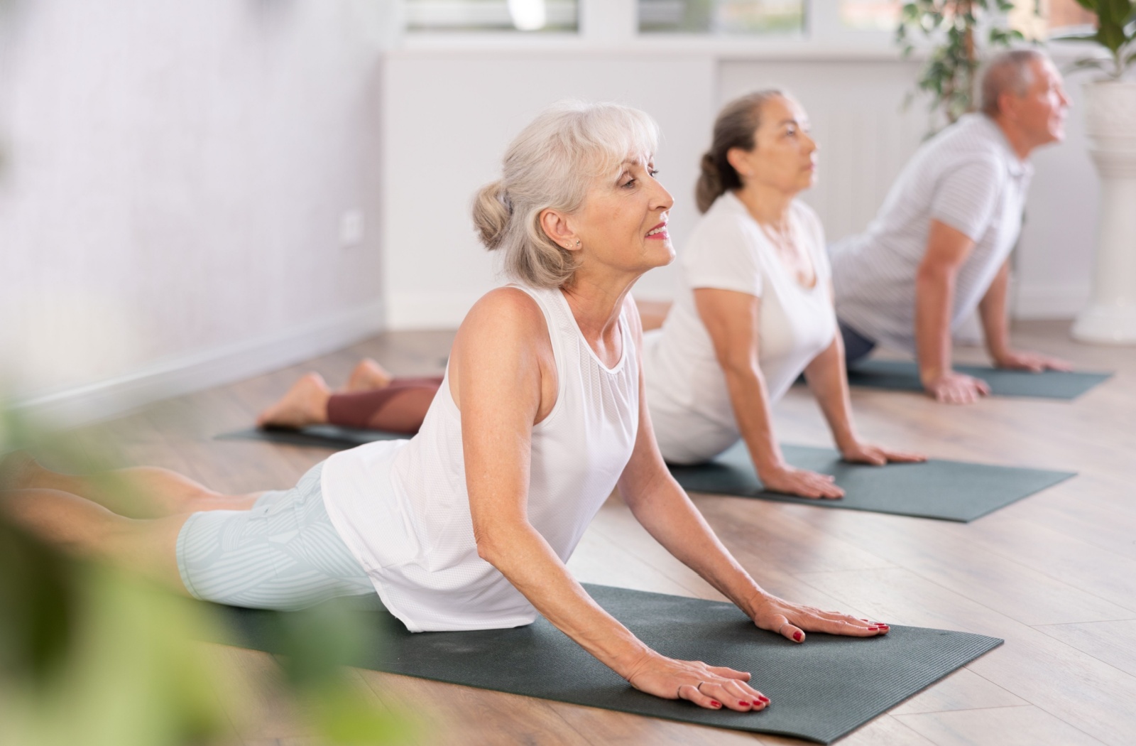 Three seniors in white follow an instructor’s guidance during a yoga class to perform a simple yoga pose and stretch