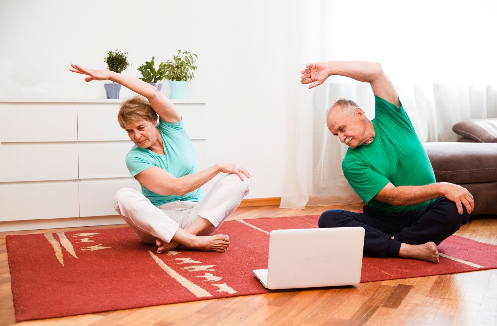 two seniors participate in a virtual seated yoga class.
