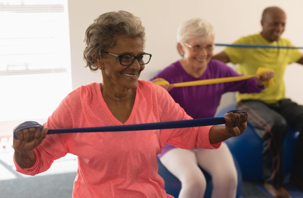 A group of three seniors sitting on exercise balls and smiling while doing band exercises