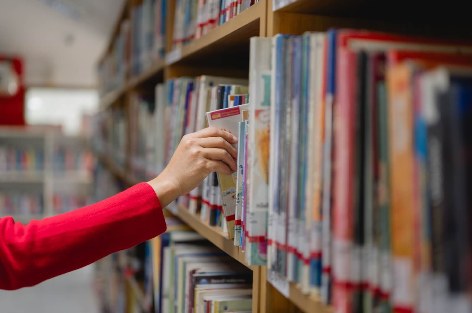 A close-up view of a hand reaching for a book on a bookshelf in a library.