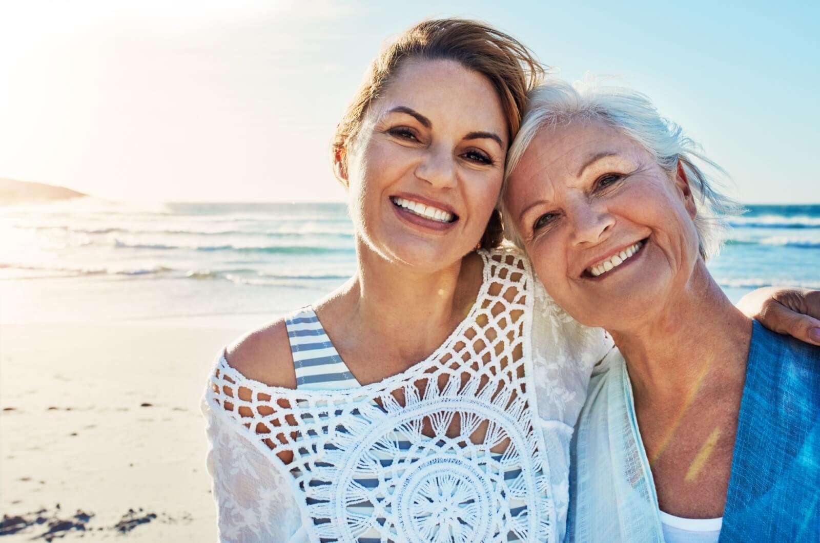 A happy adult child and their mother on the beach.