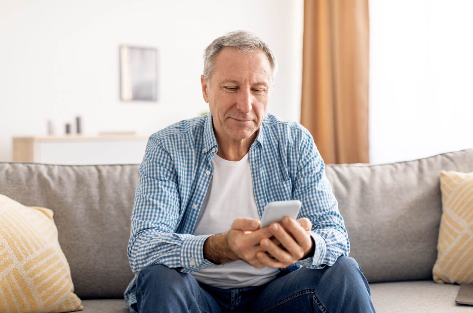 An older adult sitting on a couch with a cell phone in their hands.