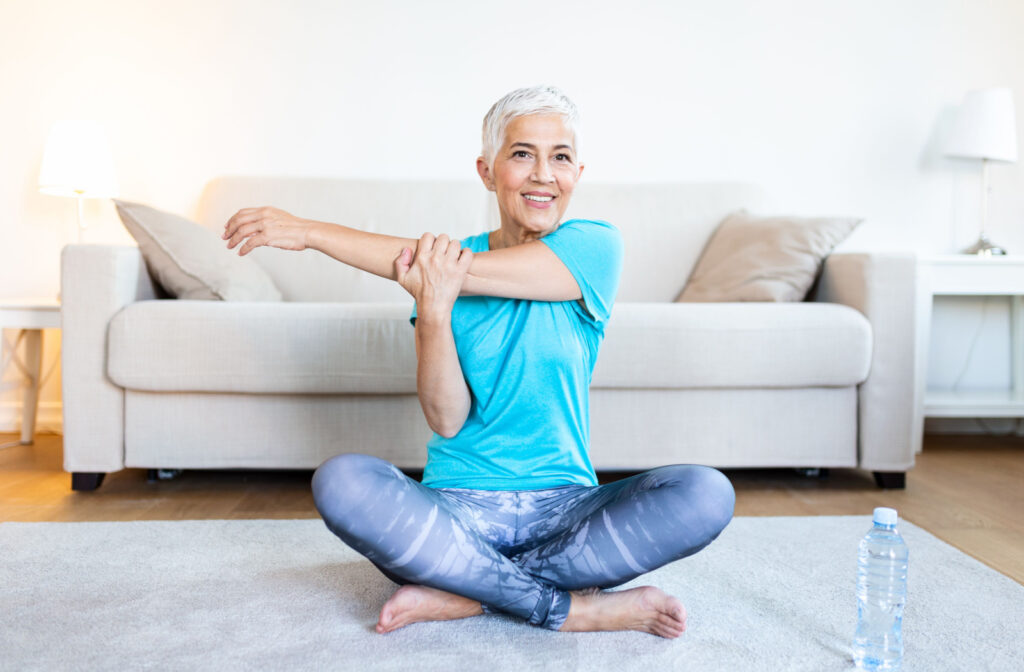 Seated on the floor, a senior lady doing arm and shoulder stretching exercises in the comfort of her home.