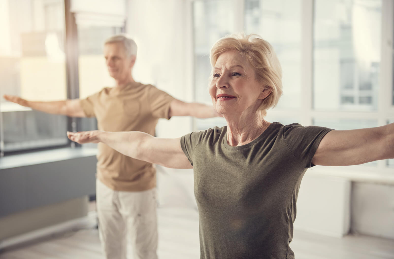 A pair of older adults stretching their arms to the side preparing for an aerobics class.