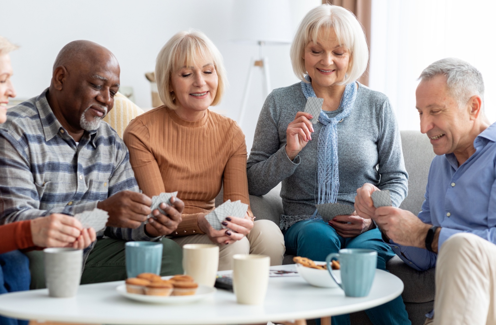 A group of seniors bonds over an afternoon tea and snack and game of cards.