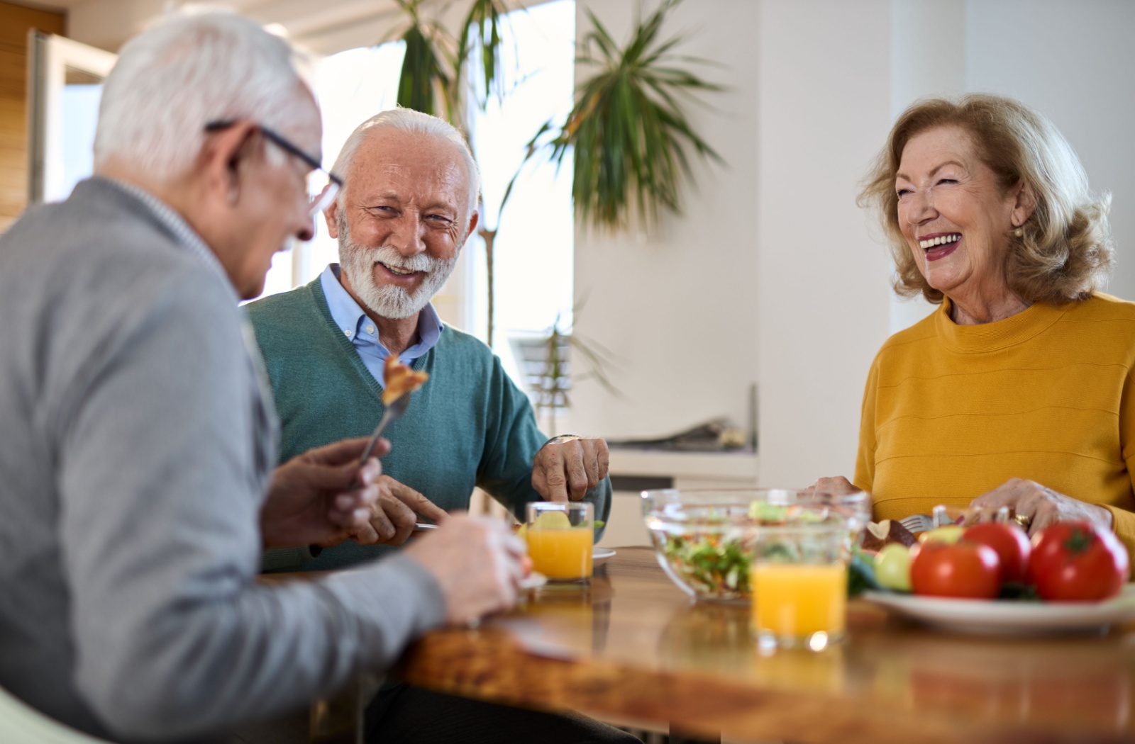 A group of seniors laughs and chats as they share a meal together.
