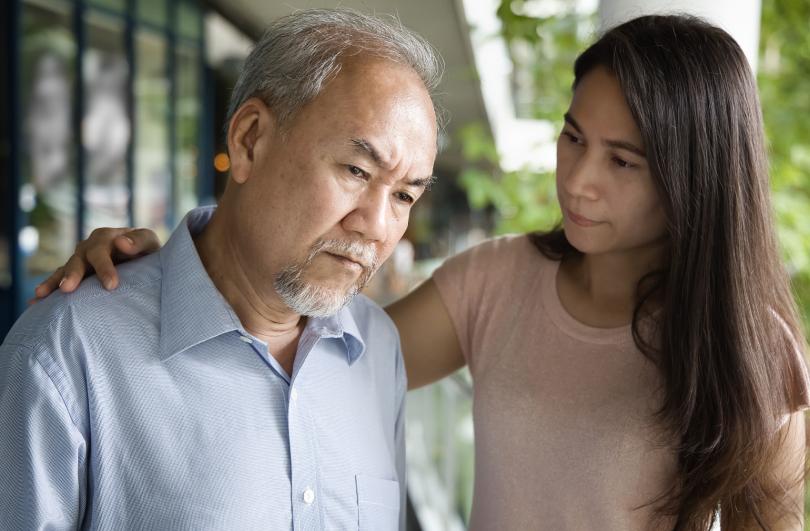 An adult child places a comforting hand on their senior parent's shoulder as they search for the right words.