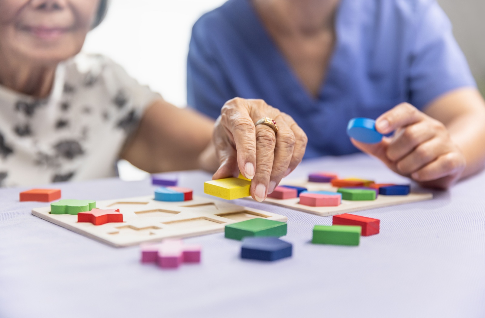 A close-up image of caregiver helping an older adult play a cognitive function-improving game.
