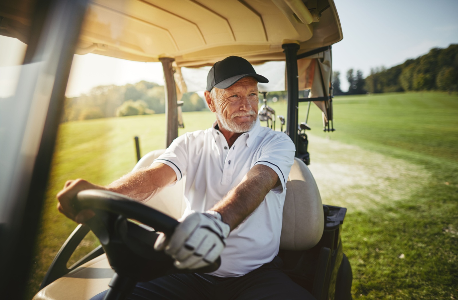 A smiling senior enjoys a cruise in their golf cart on a golf course.